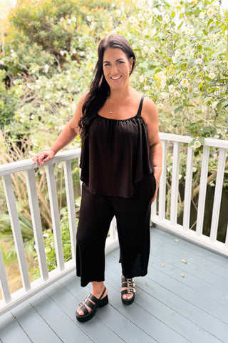 Bianca wearing the Voyager Jumpsuit in Black knit with the cape under the arms, front view — Libertine The Label