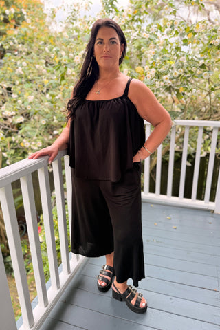 Bianca in the Voyager Jumpsuit in Black knit with the cape slipped down under the arms, wide cropped leg — Libertine The Label