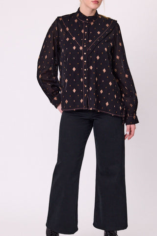 Person wearing a black patterned blouse and black pants on a white background