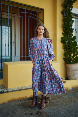 Woman in a plaid dress standing in front of a yellow building with a plant.