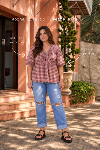 A woman wearing a marshmallow and choc latte seersucker cotton blouse with a V ruffle neckline, neck ties and wide bell sleeves to the elbow.