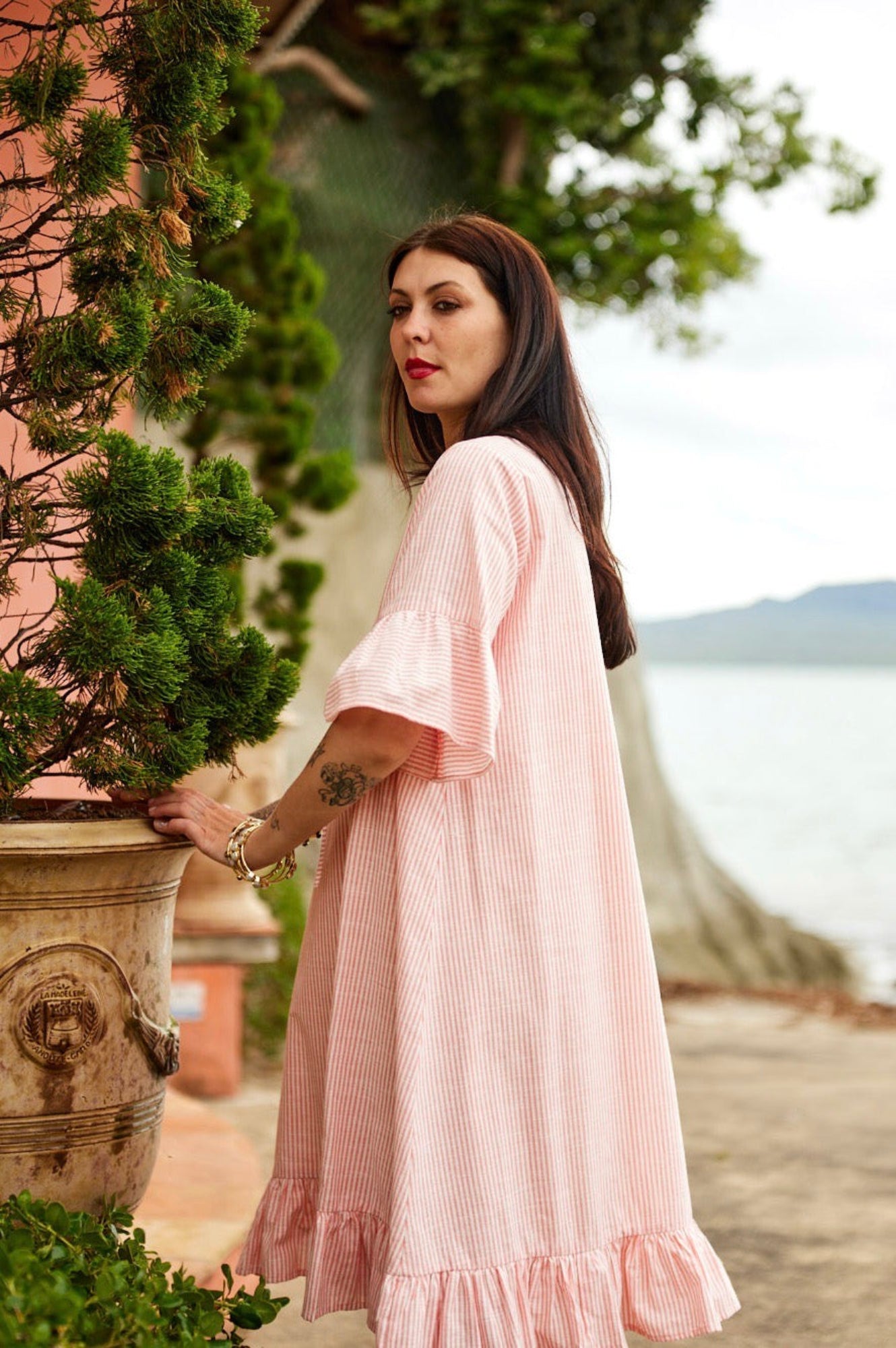 Woman in a pink dress standing by a potted plant with a scenic background