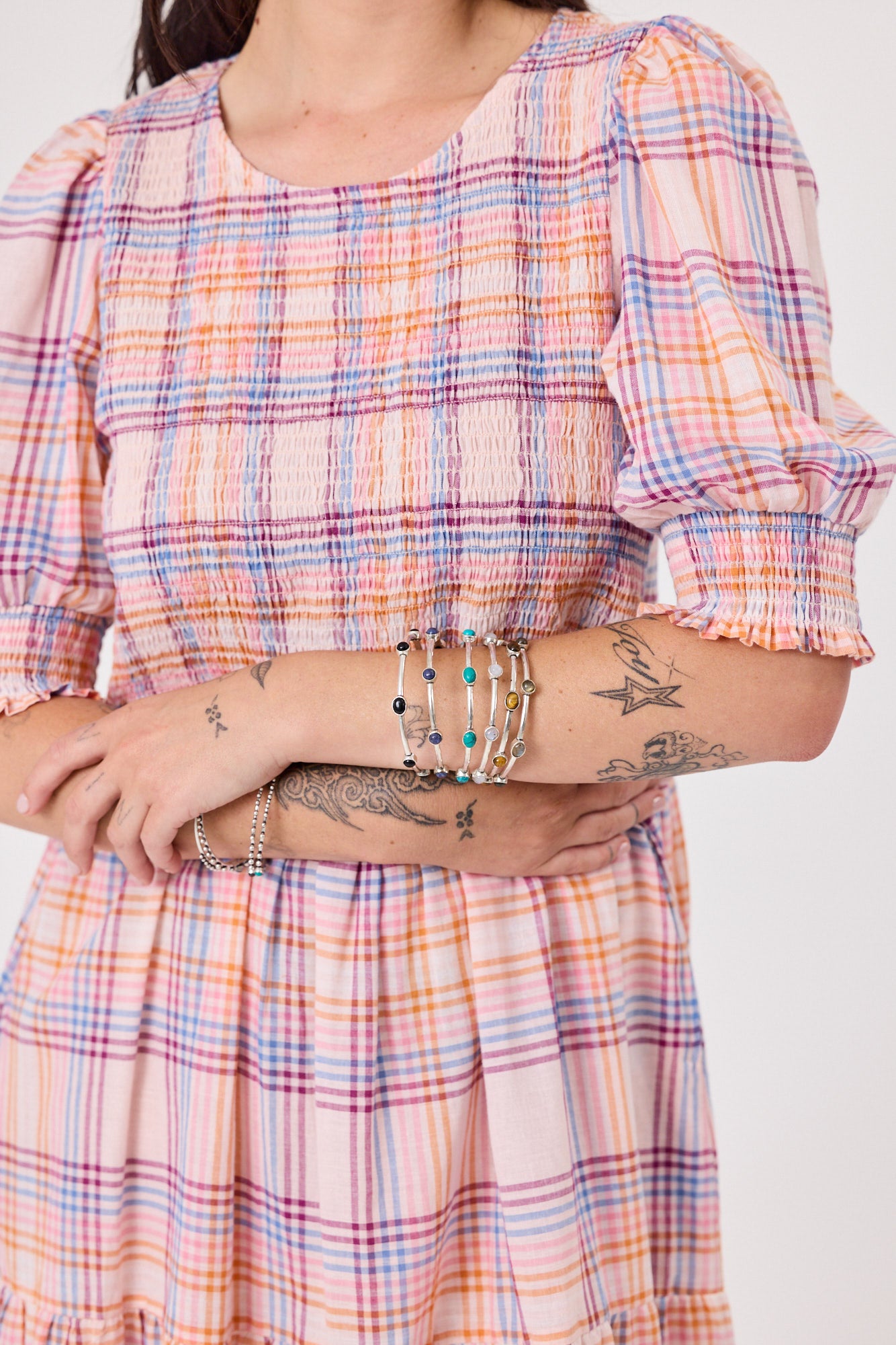 Person wearing a plaid dress with visible tattoos and bracelets on a white background