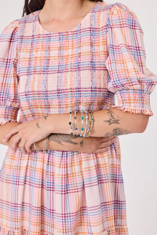 Person wearing a plaid dress with visible tattoos and bracelets on a white background