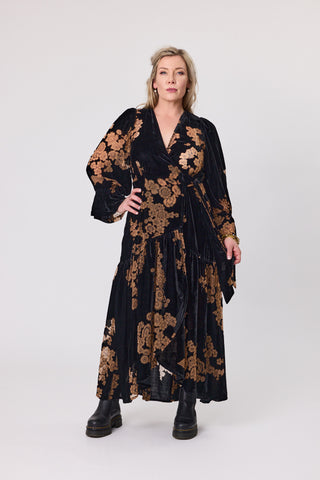 Woman wearing a black dress with gold floral patterns on a white background