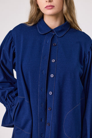 Blue shirt with long sleeves and a collar worn by a person on a white background