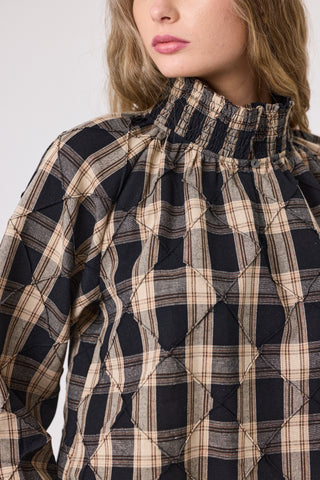 Close-up of a person wearing a black and beige plaid shirt with a high collar.
