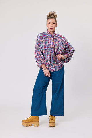 Model wearing a stylish shadow blouse in French tartan cotton paired with blue wide-leg pants and yellow platform shoes.