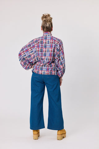 Back view of a model wearing a shadow blouse in French tartan, paired with blue wide-leg pants and yellow platform shoes.