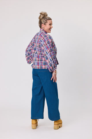 Model wearing a stylish Shadow Blouse in French Tartan fabric, paired with blue wide-leg pants.