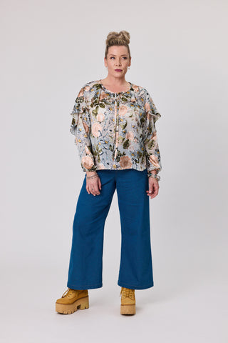 Woman wearing a floral blouse and blue pants on a white background