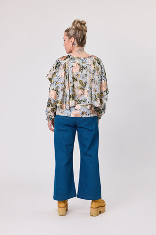 Woman wearing a floral blouse and blue pants on a white background