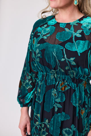 Model showcasing the teal orchid velvet dress featuring vibrant floral patterns and an elasticated empire waist.