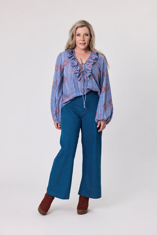 Woman wearing a blue embroidered cross stitch blouse and blue flared pants on a white background
