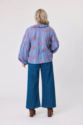 woman wearing a blue embroidered blouse and blue jeans on a white background