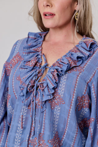Woman wearing a blue embroidered blouse with ruffled neckline.
