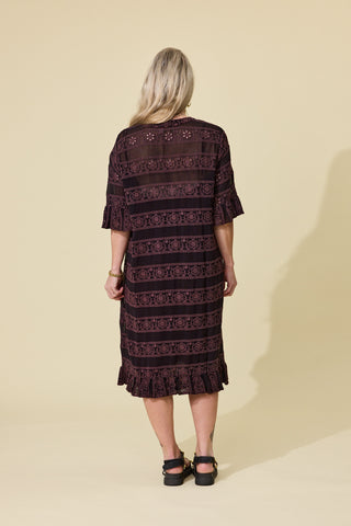 A woman modeling a dark espresso embroidery lace-up dress with ruffled sleeves and hem, paired with black platform sandals, against a solid beige studio background.