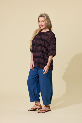 A woman modelling a espresso embroidered short-sleeve top and blue barrel jeans against a solid beige studio background.