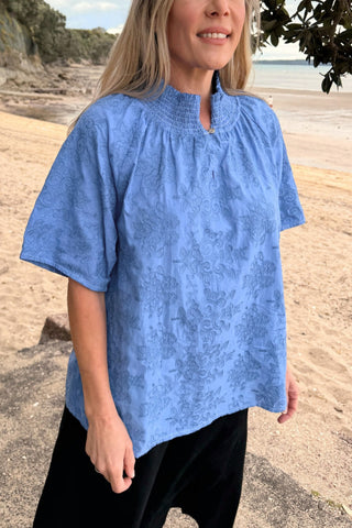 Evana wearing the Dylan Blouse in Cornflower embroidery, worn loose on the beach — Libertine The Label
