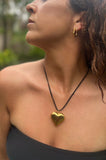 Woman wearing a gold heart-shaped necklace with a blurred natural background