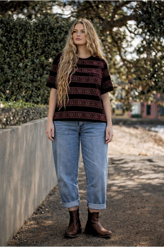 Woman wearing a embroidered top and jeans standing outdoors with trees in the background