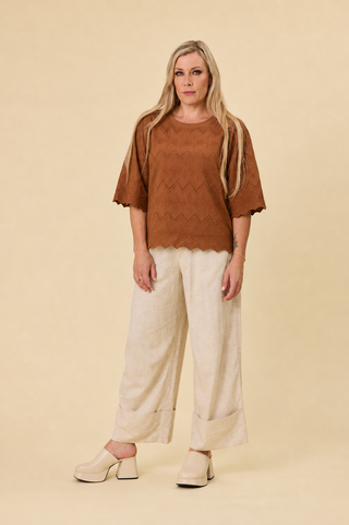 A woman modeling a hazelnut luna lace top short-sleeve top and sahara barrel-leg champagne pants against a solid beige studio background - Libertine the label