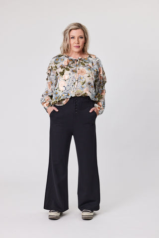 Woman wearing a floral blouse and black pants on a white background