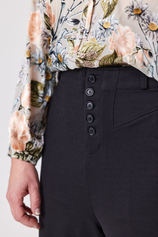 Person wearing a floral blouse and black pants with buttons.