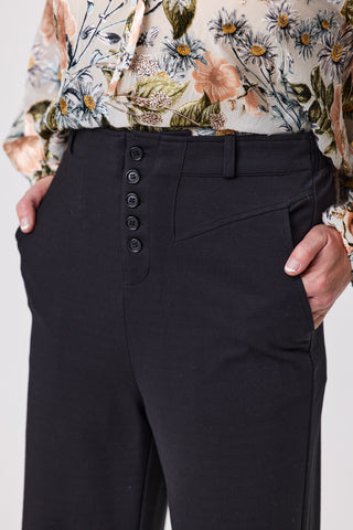 Black pants with button details worn by a person, with a floral top partially visible.
