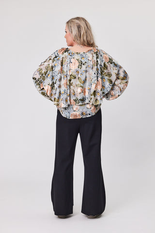 Woman wearing a floral blouse and black pants on a white background